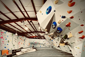 White bouldering walls with various multi-colored holds surrounded by padded floors.