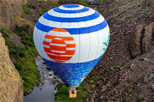 Hot air balloon flying over stream inside canyon.