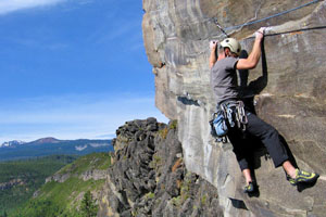 Climber high on a face of Smith Rock with mountains in the background.