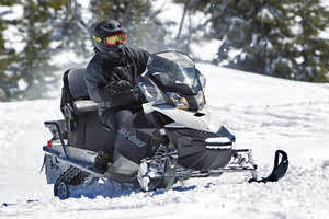 Snowmobile speeding across snowfield with snow-covered trees in the background.
