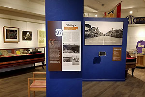 Exhibit concerning U.S. Highway 97 with photographs and display cases in the background.