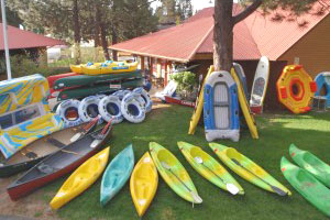 Kayaks, rafts, tubes, canoes, and stand up paddle boards displayed on a lawn with the storefront in the background.