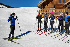 Nordic ski instructor on the left facing a row of students on the right with the Nordic Center in the background.