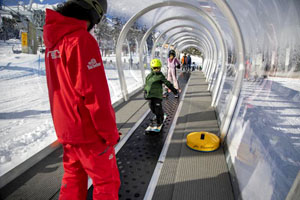 Instructor with young snowboard students on a walking carpet