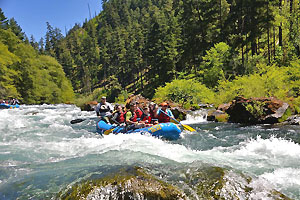 Group of people in a blue inflatable raft on a river and paddling through whitewater.