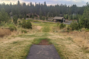 Disc golf hole with the tee in the foreground, the target in the background, and a mowed grass fairway in between.