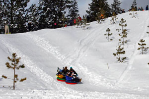 Family sliding down the small tubing hill with a line of people waiting at the top.