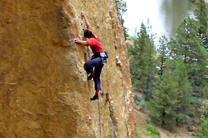 Climber high up on the Captain Xenolith route of Smith Rock with the Crooked River in the background.