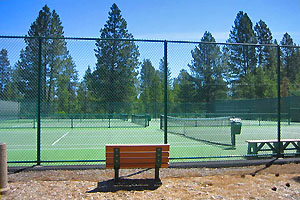 Sunriver tennis courts with wood bench in the foreground and pine trees in the background.