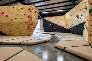 Wood panel bouldering walls with various multi-colored holds surrounded by padded floors.