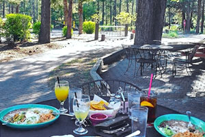 Outdoor table holding two plates of food and drinks with trees and bike rack in the background.
