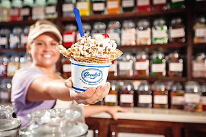 Employee holding ice cream filled waffle dish with counter and shelves of hard candies in the background.