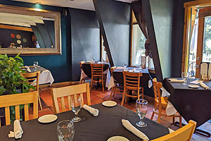 Interior with tables including several along windows overlooking an outdoor deck.