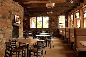 Interior of the restaurant with tables, booths, and a large stone fireplace running along the left.