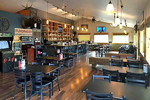 Interior with tables adjacent to windows along the right and a bar to the left in the background.